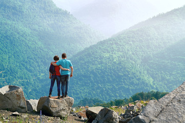 Happy couple standing embraced on the cliff edge and enjoying beautiful morning view in the mountains