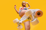 Bottom view of roller skate step on camera, cheerful joyful playful funky girl showing equipment for fitness workout isolated on yellow background