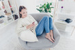 © deagreez - High angle view of cute addicted blogger in jeans sweater sitting on chair in modern living room with interior having smart phone in hands using wi-fi 3G internet