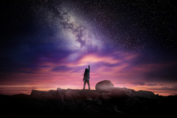 night time long exposure landscape photography. a man standing in a high place reaching up in wonder