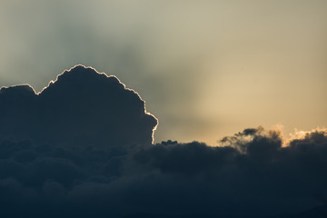 Sun hidden behind dark clouds on sunset. Ray of light. Copy space. Background.