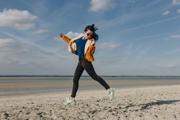 stylish girl in sunglasses jumping on sandy beach, Saint michaels mount, France