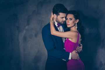 Wall Mural - Portrait of lovely romantic couple embracing, pretty mrs jewelry, rich harsh mr with bristle in tux with bowtie enjoying smell of lover isolated on grey background. Betrayal adultery perfume concept