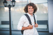 © iuricazac - Handsome happy young student guy with backpack on the city street. Caucasian male with curly hair, smiling and looking at the camera in white shirtt is going to university.People and lifestyle concept
