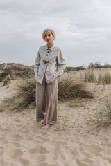 Wall Mural - stylish young woman in retro jacket on sand dune under cloudy sky