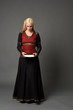 © faestock - full length portrait of pretty blonde lady wearing  a red and black fantasy medieval gown, holding a book. standing pose on grey background.