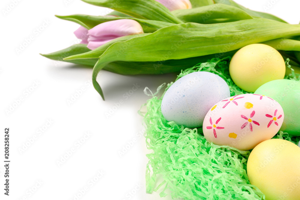 Decorative nest with dyed Easter eggs and spring flowers on white background