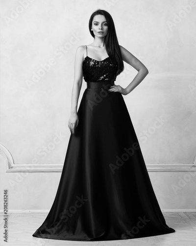 Charming Brunette Woman Dressed In Formal Maxi Dress With Top Decorated With Black Sequins And Purple Satin Bottom Female Model Posing In Elegant Evening Gown Against White Wall On Background Stock Photo