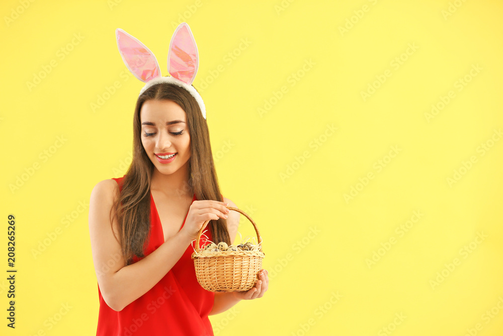 Beautiful young woman with Easter eggs and bunny ears on color background