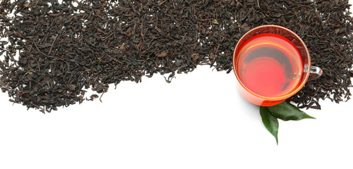 Dry black tea leaves and cup of aromatic beverage on white background