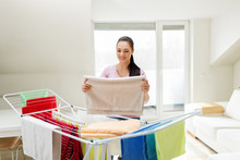 Laundry And Household Concept - Happy Woman Or Housewife Taking Bath Towels From Drying Rack At Home