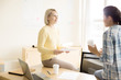 © pressmaster - Young blonde female talking to brunette sitting on table with papers laptop and cups