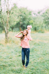 Mother and little daughter playing together in a park. Happy cheerful family. Mother and baby kissing, laughing and hugging in nature outdoors