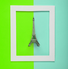 Wall Mural - Souvenir statuette of the Eiffel tower in a white frame on a colored background. Minimalist trend. Top view..