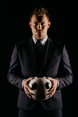 Wall Mural - young handsome businessman holding a football on black background studio.