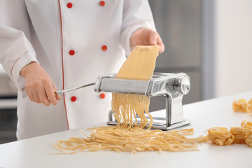 Female chef making noodles with pasta machine at table