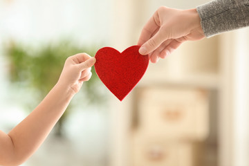 Hands of little girl and her mother holding red heart against blurred background