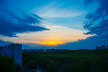 Wall Mural - atmospheric blue cloudy sky behind silhouettes of city buildings. cobalt and orange background of su