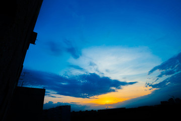 Wall Mural - atmospheric blue cloudy sky behind silhouettes of city buildings. cobalt and orange background of su