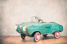 Retro Outdated Rusty Metal Turquoise Pedal Car Toy From Circa Late 60s Or Early 70s In Front Concrete Textured Wall Background. Vintage Style Filtered Photo