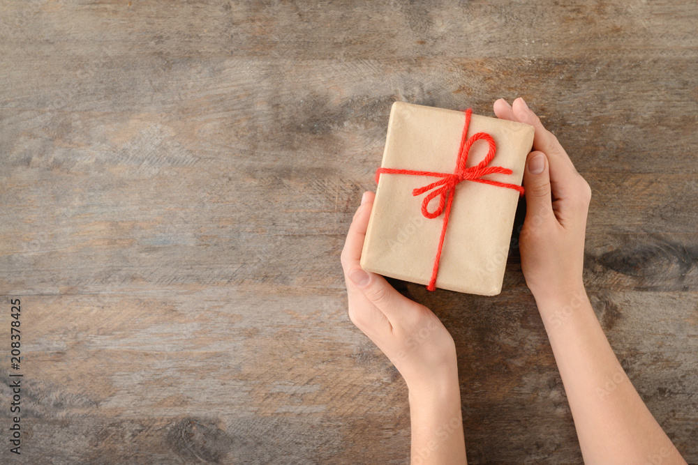 Woman holding gift box on wooden background, top view