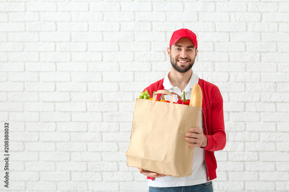 Delivery man holding paper bag with food on brick wall background
