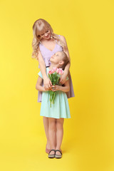 Portrait of cute little girl and her mother with tulip bouquet on color background