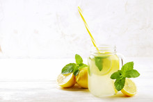 One Mason Jar Glass Of Homemade Refreshing Lemonade With Slices Of Organic Ripe Lemon, Whole And Halved. Non Alcoholic Beverage On A Rustic White Wooden Background. Close Up, Top View, Copy Space.