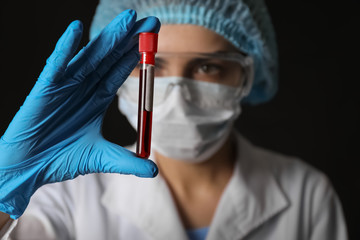 Lab worker holding test tube with blood sample on black background