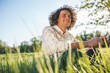 © iuricazac - Outdoor shot of happy handsome young male with curly hair smiling and looking a side, sitting on the green grass in the park, relaxing after busy day. Copy space for advertising. People, lifestyle
