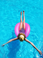 Wall Mural - Young beautiful girl relaxing and swimming in the blue swimming pool with a pink circle closeup