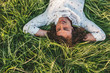© iuricazac - Portrait from above of handsome young male with curly hair smiling and lying with hands behind head on the green grass in the park, looking at the sky. Copy space for advertising. People, lifestyle.