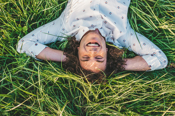 portrait of happy handsome young male with curly hair smiling and lying with hands behind head on th