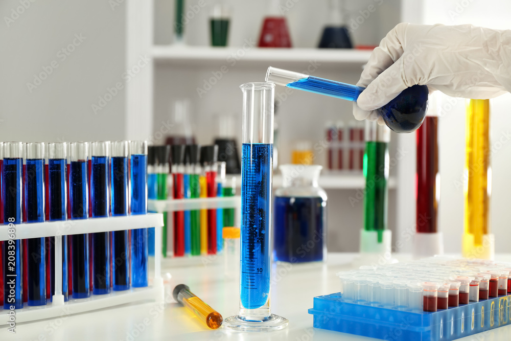 Lab worker pouring blue liquid into test tube on table