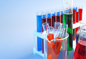 Chemical glassware with different liquids on color background