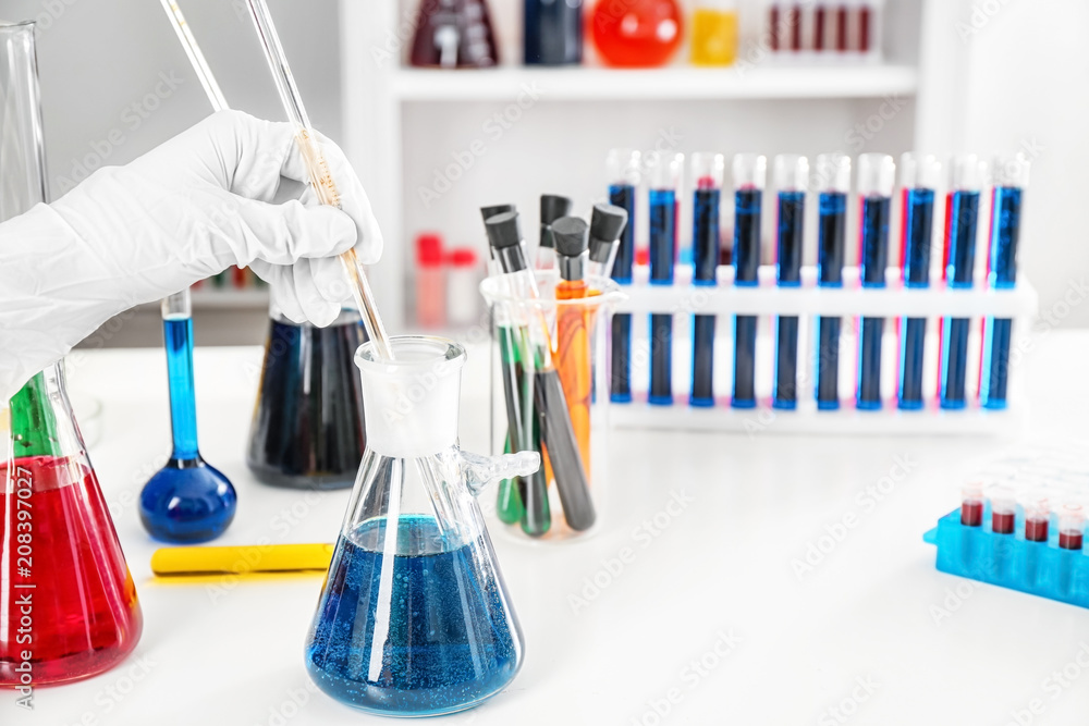Lab worker taking sample from test tube with blue liquid on table