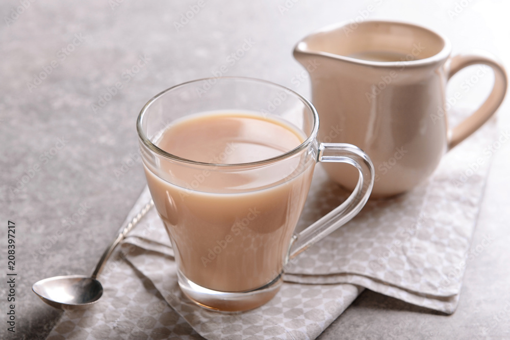 Glass cup of aromatic tea with milk on table