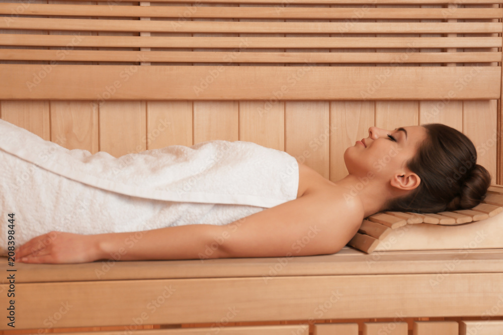 Young woman lying on wooden bench in sauna