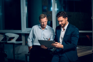 two office collegues looking at tablet. handsome businessman wearing suit showing something to his c