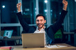 © Svyatoslav Lypynskyy - Cheerful businessman with his hands up sitting behind computer. Happy businessman wearing suit raising both of his hands up after completing work in office at late hour.