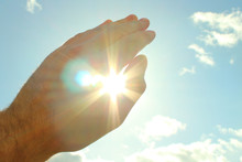 A Man's Hand Covers A Bright Scorching Sun. The Sun Shines Through And Dazzles Through The Hand. Close-up. Background.