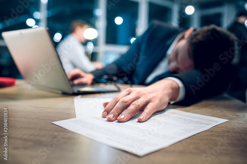 Hand Of Sleeping Businessman Lying On Pile Of Papers Exhausted