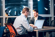 © Svyatoslav Lypynskyy - Working men sitting at table with their computers. Senior businessmen sittting at office desk working on laptop with his younger colleague sitting in background.