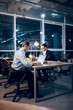© Svyatoslav Lypynskyy - Two coworkers finishing up on some work in late hour. Businessmen sitting at desk facing each other working on project at nighttime in their office.