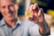 © Svyatoslav Lypynskyy - Cryptocurrency bitcoin coin in mans hand. Close picture of golden bitcoin being held by smiling man in button down shirt.
