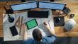 © Gorodenkoff - Top View of Architectural Engineer Draws on His Blueprints, Compares with Tablet Computer with Green Screen, Using Desktop Computer Also. His Desk is Full of Useful Objects and Evening Sun.