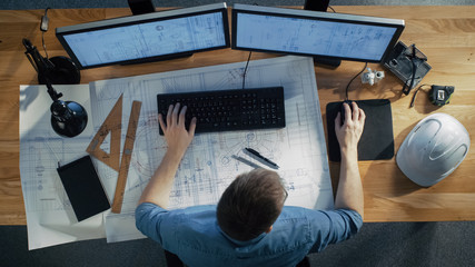top view of architectural engineer working on his blueprints, holding tablet computer, using desktop
