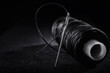 Needle and bobbin with black thread on black background