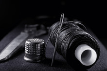 Needle With Thread, Thimble, Bobbin With Black Thread And Scissors On Black Background