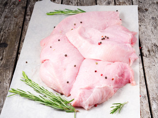 Raw turkey fillet chops with fresh rosmary on a old rustic gray wooden background. Top view.